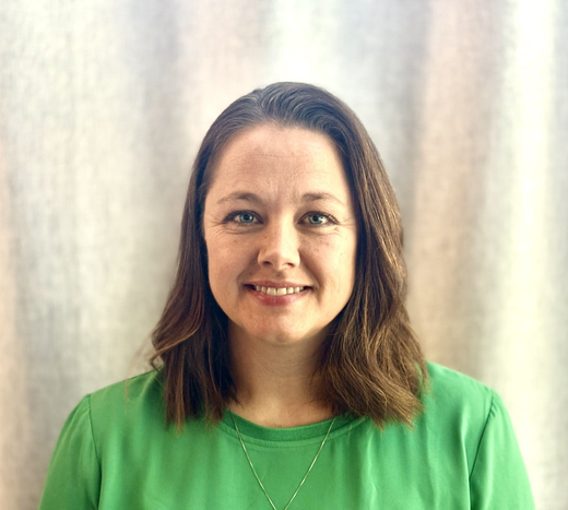 Woman with brown hair in a green shirt smiles against a white backdrop.