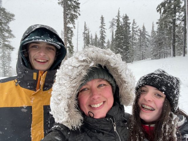 Family smiles in snowy weather, wearing winter coats and hats in a forest.