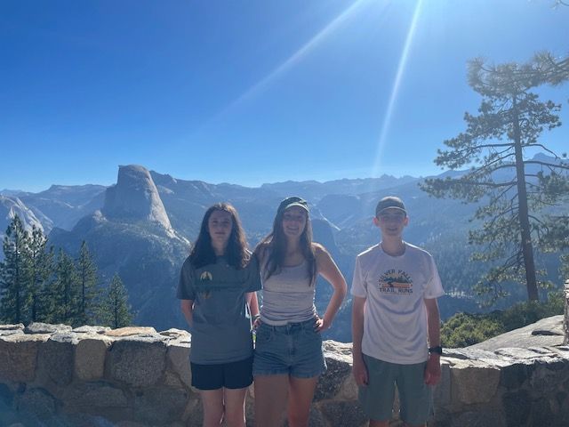 Three people pose with Half Dome in the background, under a bright blue sky.