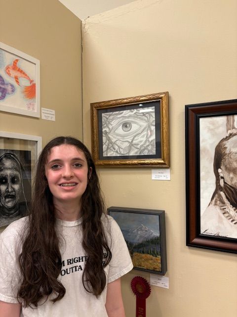 Teen girl with braces stands by her artwork in an art show.