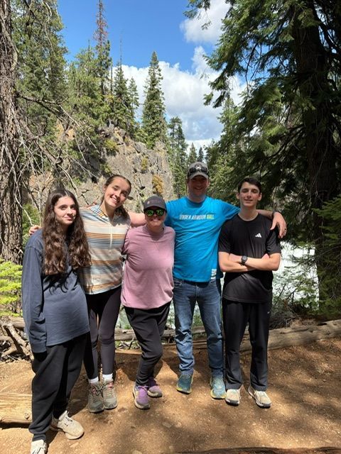 Family of five poses outdoors near a rocky ledge and waterfall. They are smiling and looking at the camera.