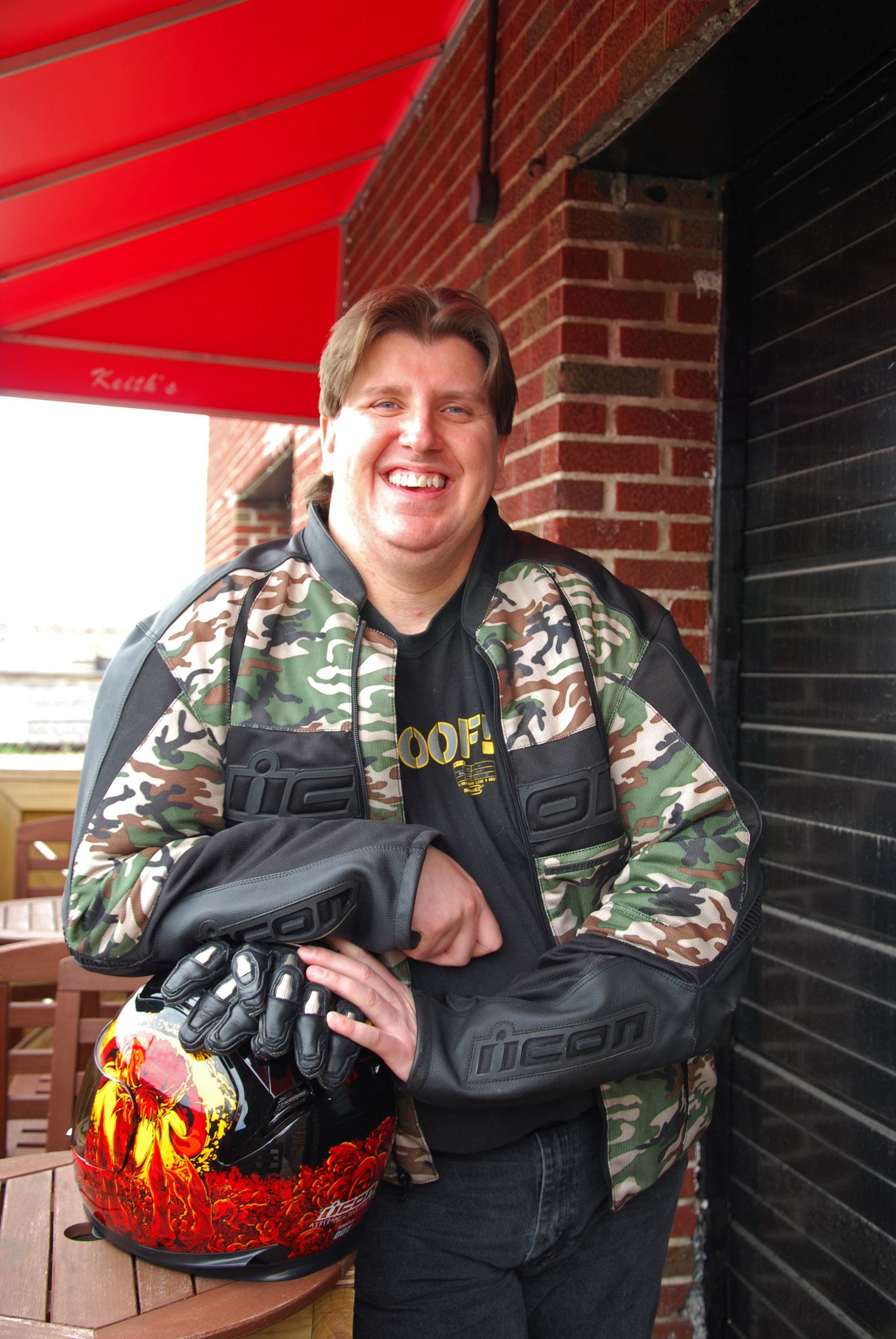 A man in a camo jacket is holding a red helmet