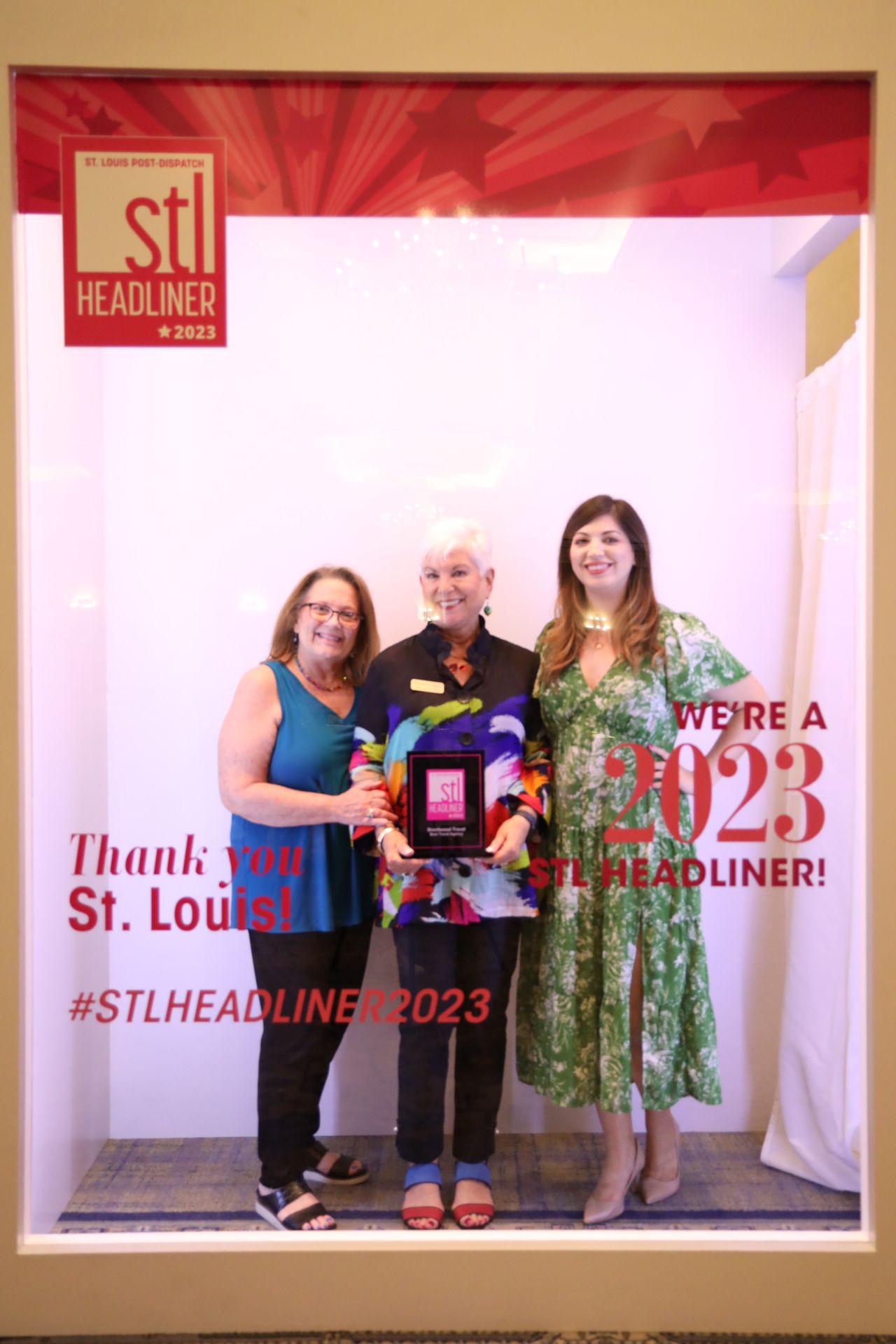 three women showcasing an award Three people are posing for a picture in front of a sign that says ' we 're a ' on it.