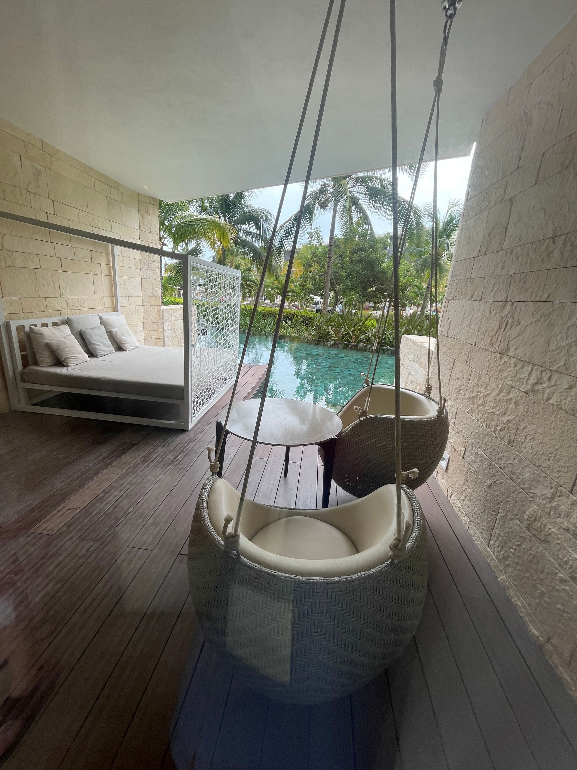 A balcony with a swing and a bed with a swimming pool in the background