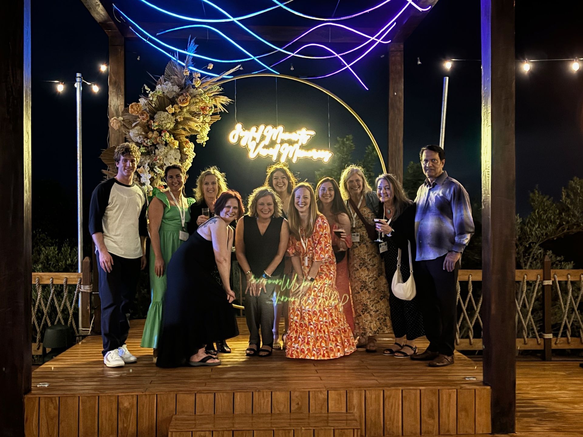 A group of people are posing for a picture in front of a neon sign.