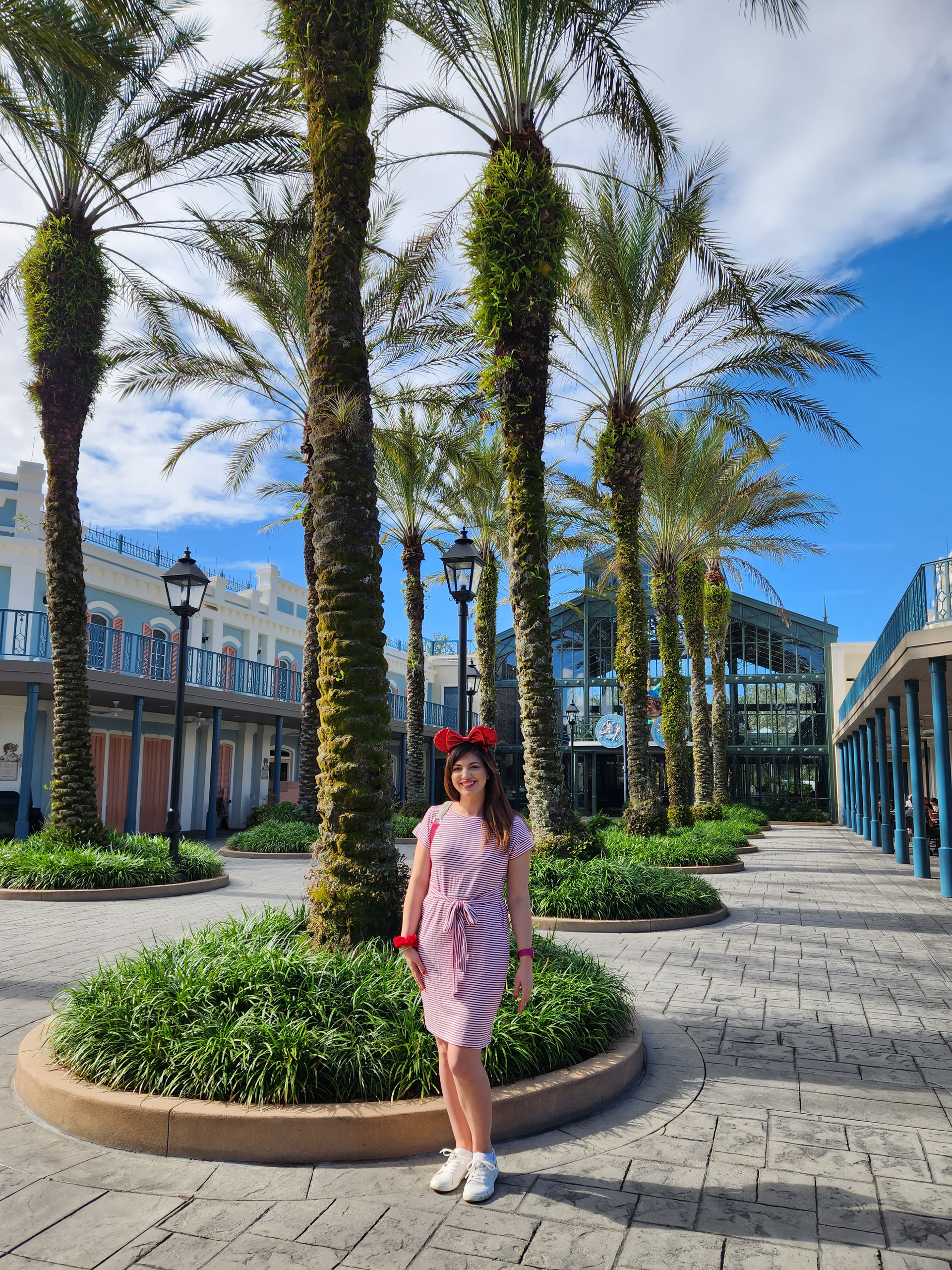 A woman in a pink dress is standing in front of a row of palm trees.