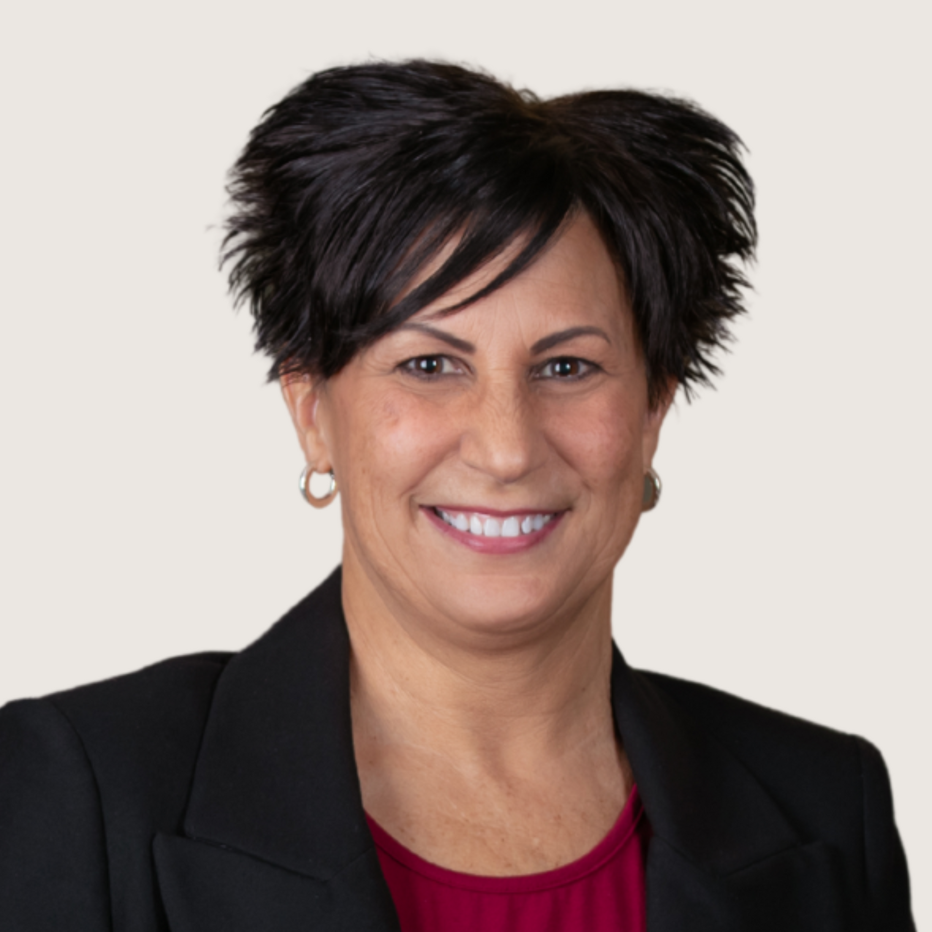 A woman in a black jacket and red shirt is standing next to a railing and smiling.