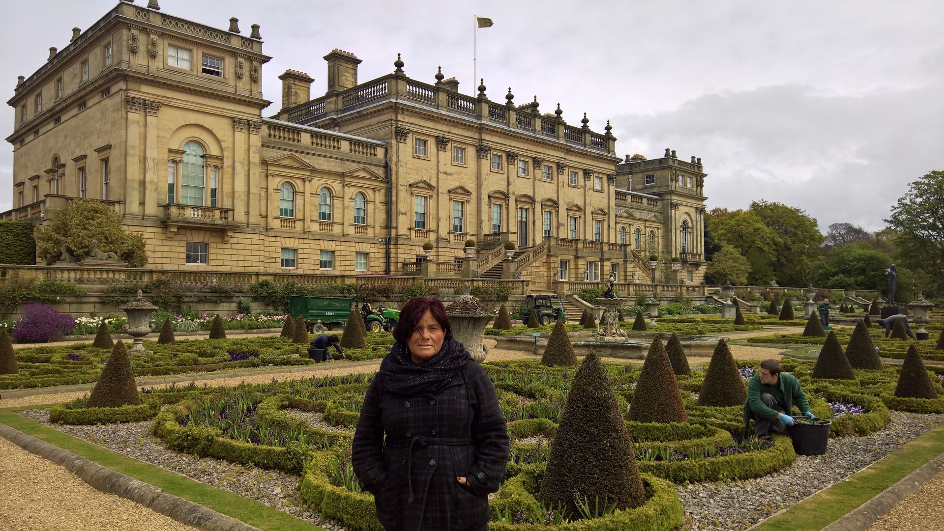 A woman is standing in a garden in front of a large building.