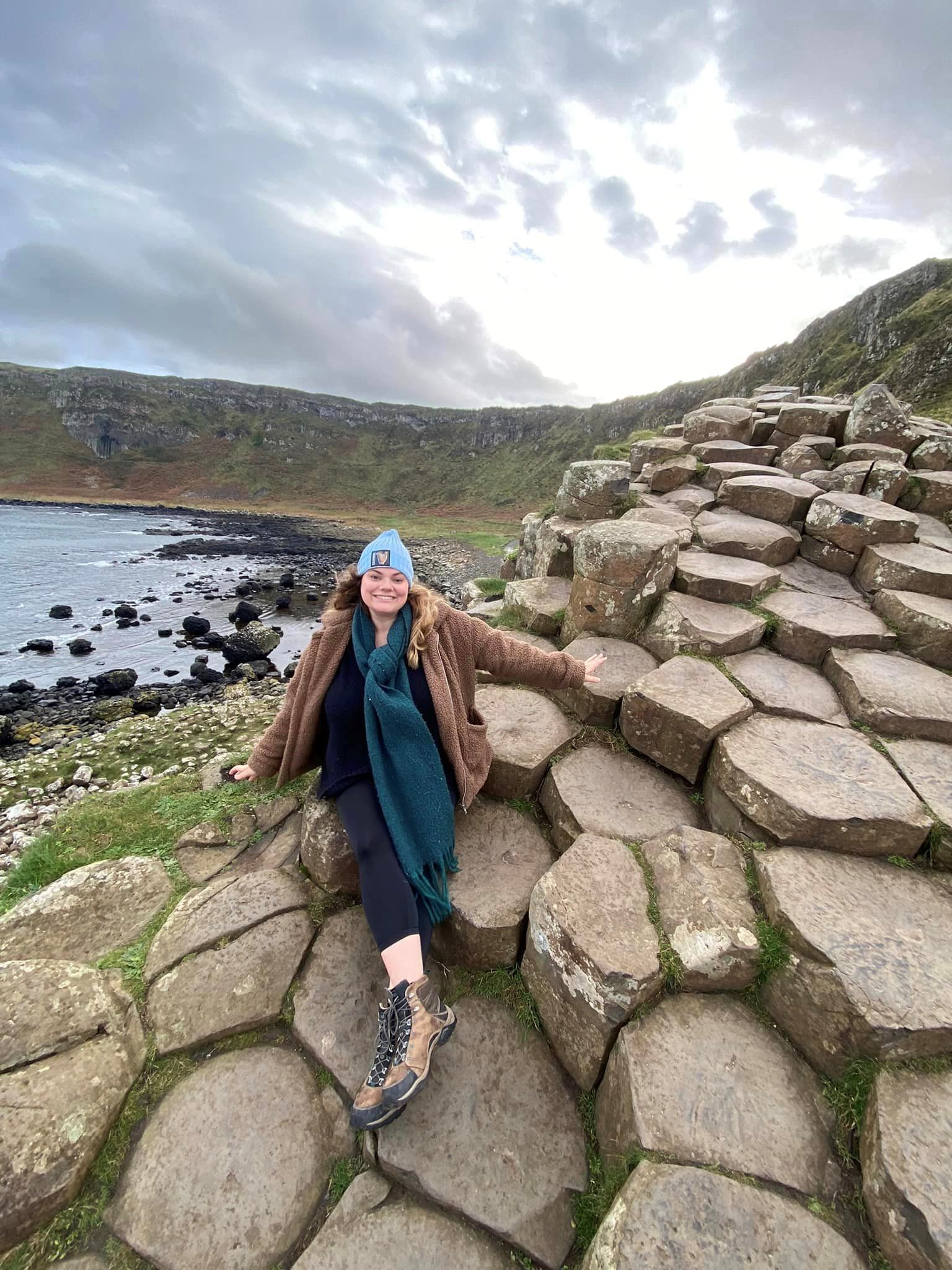 A woman is sitting on a pile of rocks next to a body of water.