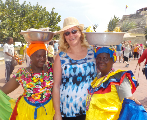 A woman in a hat is standing next to two women carrying bowls on their heads