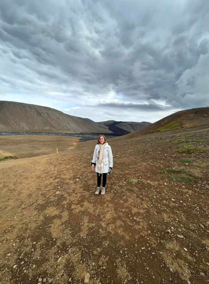 A woman in a white coat is standing in the middle of a dirt field.