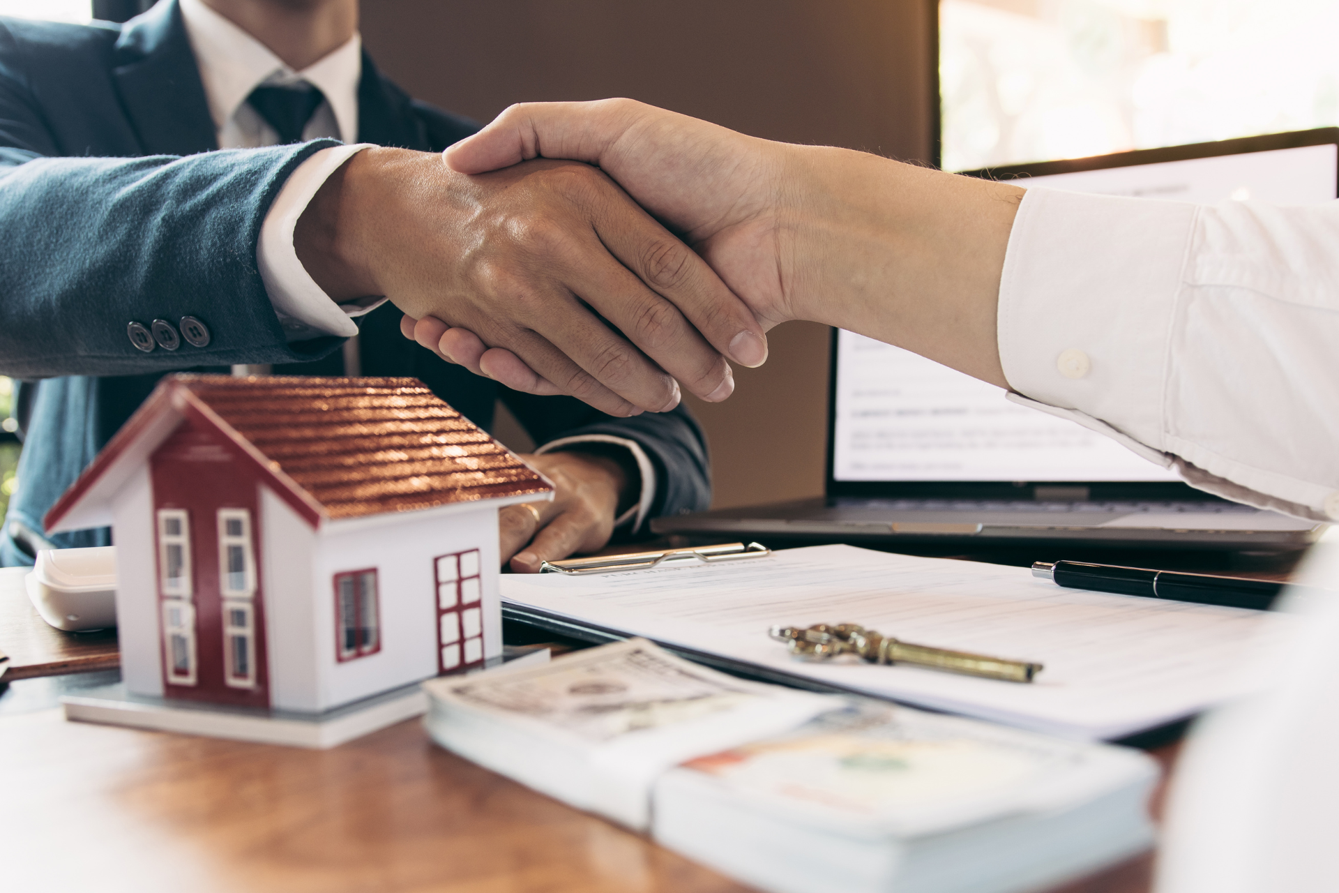 A man in a suit and tie is shaking hands with a woman in front of a model house.