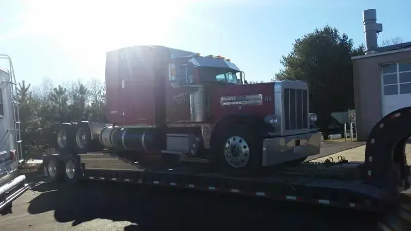 A red semi truck is sitting on top of a flatbed trailer.