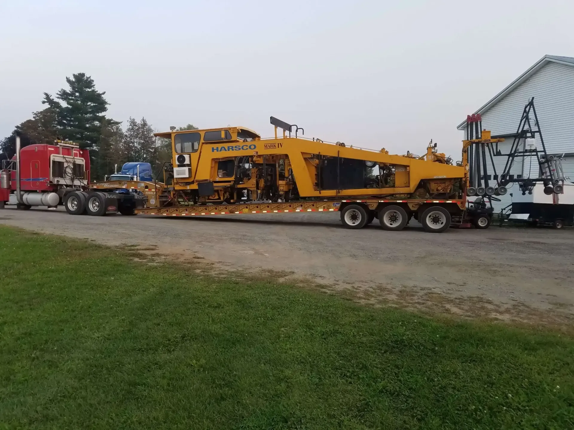 A truck is carrying a large yellow tractor on a trailer.