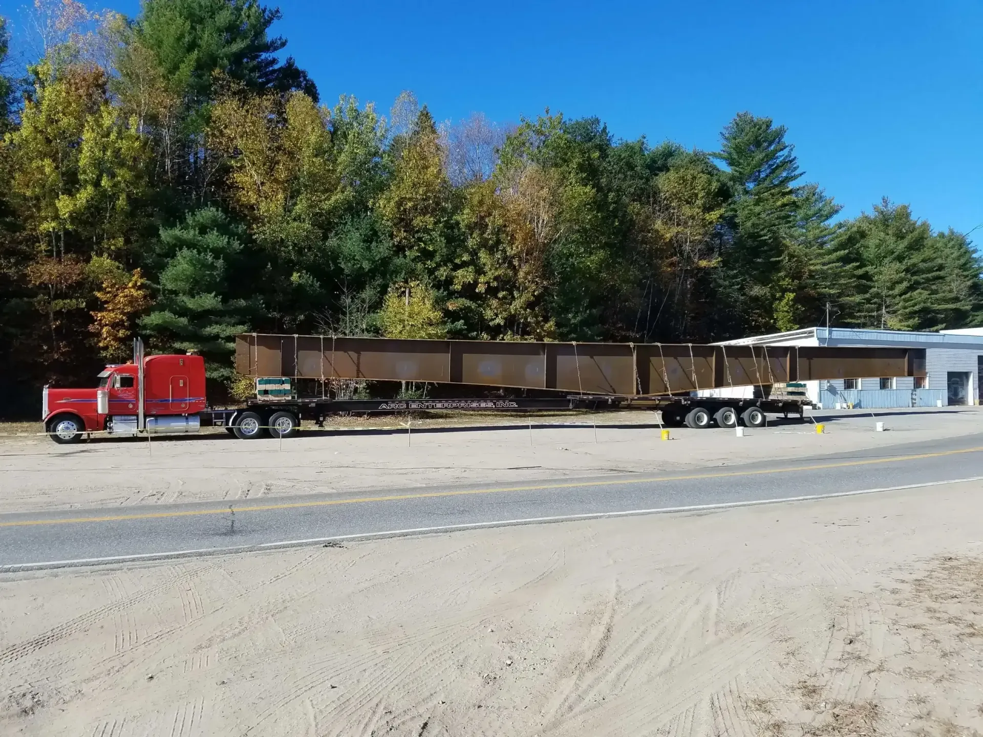 A red semi truck is pulling a train car down a dirt road