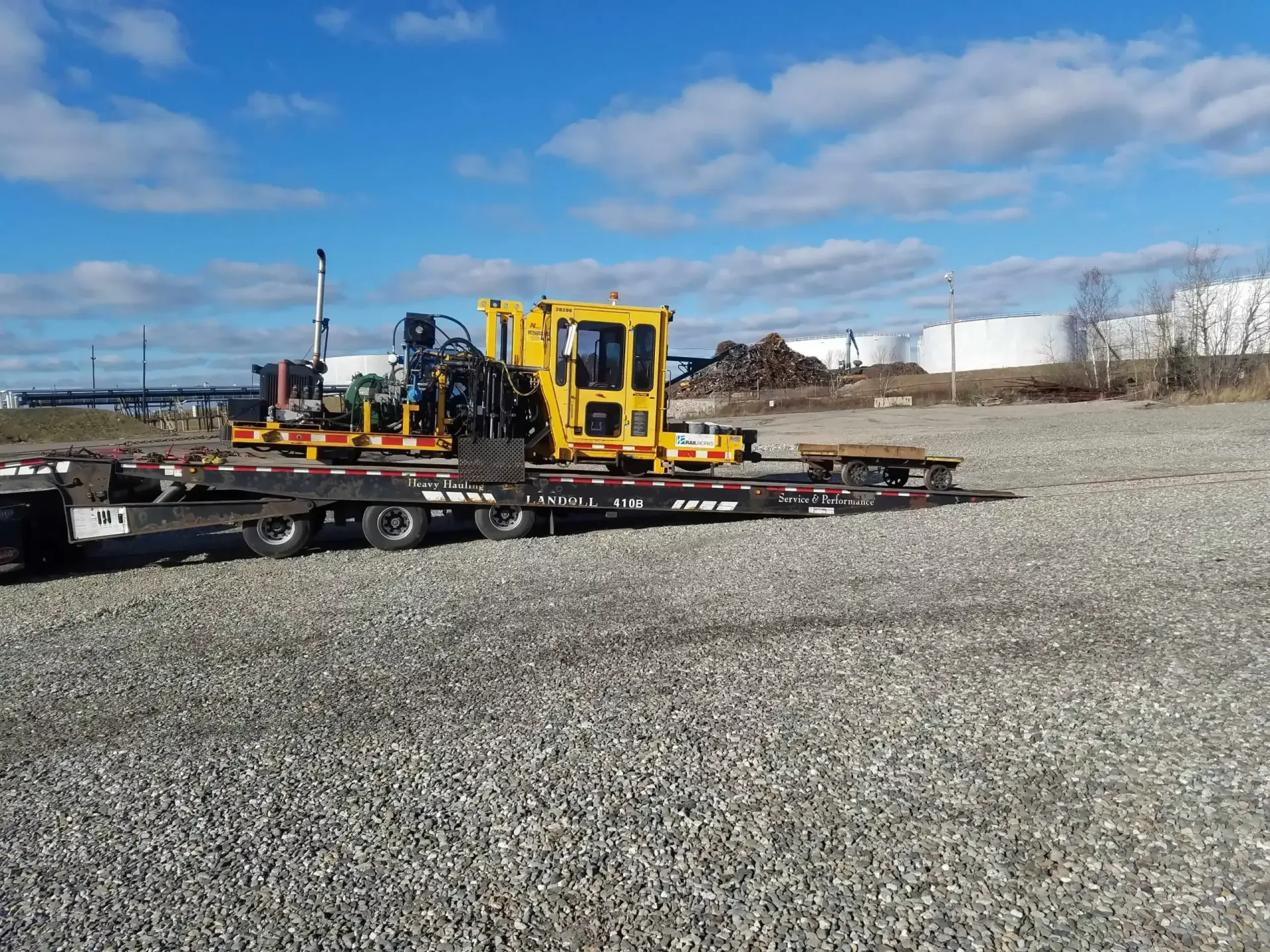 A yellow tractor is sitting on top of a trailer in a gravel area.