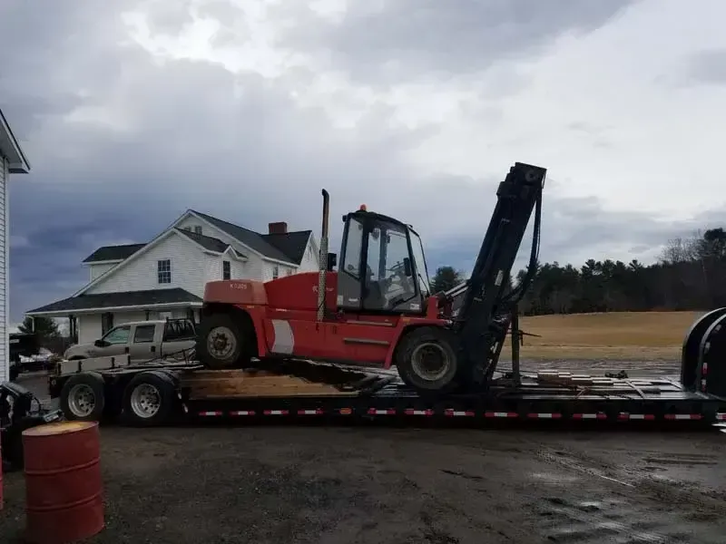 A red forklift is sitting on top of a flatbed trailer.