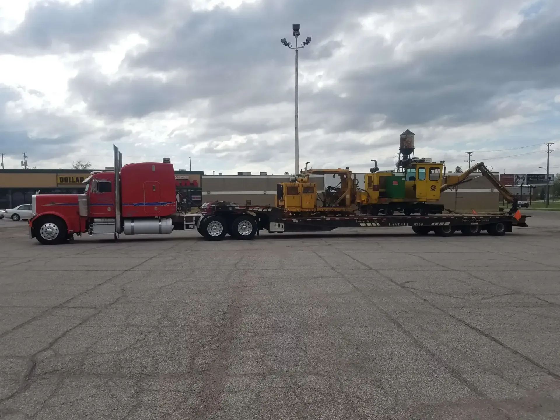A red semi truck is pulling a yellow excavator on a trailer