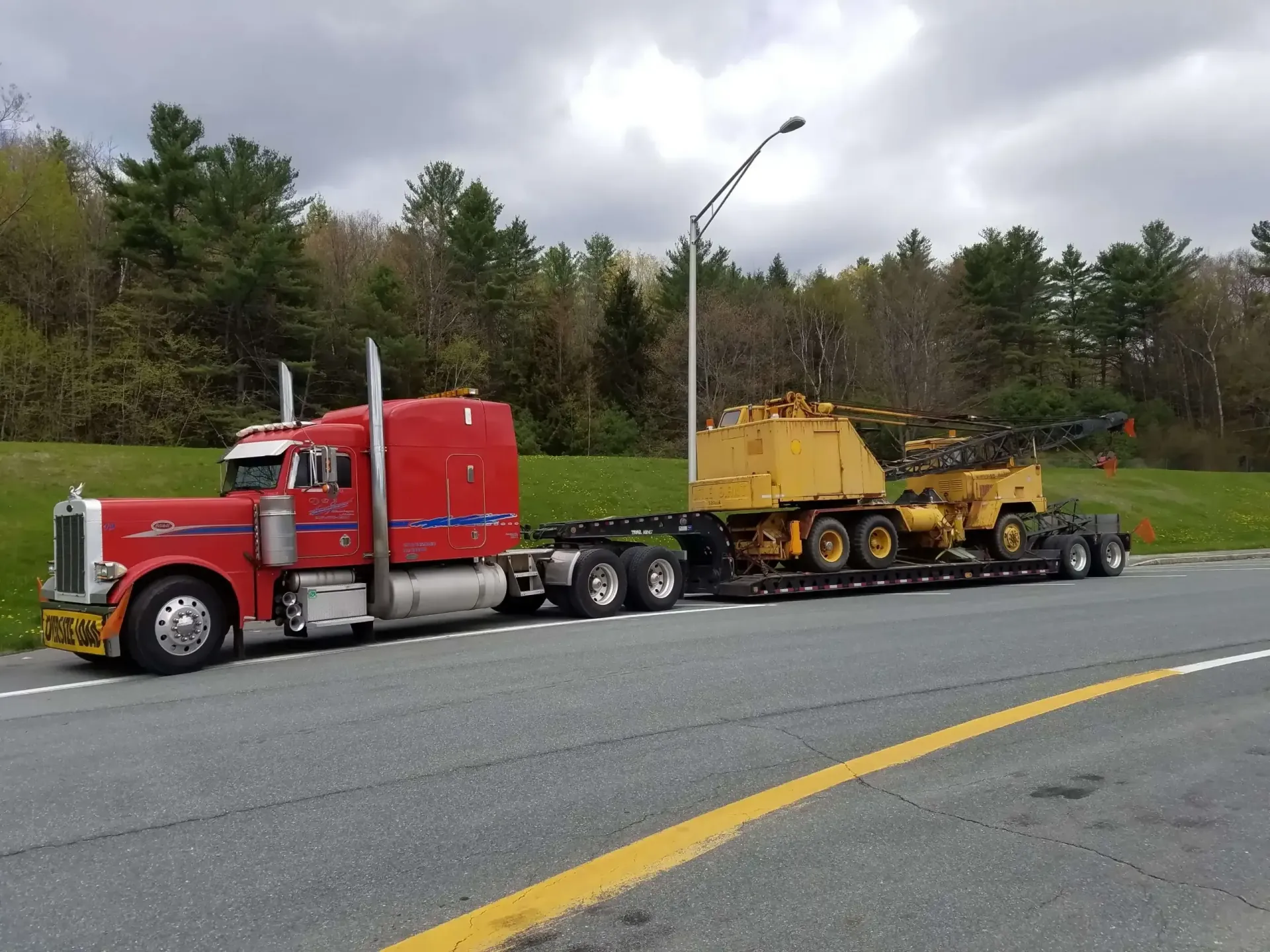 A red semi truck is pulling a yellow bulldozer down a road.