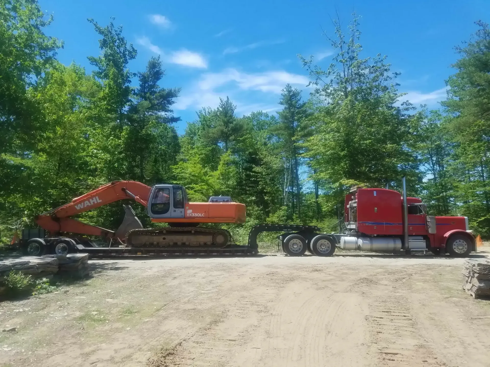 A red semi truck is carrying a large excavator on a trailer.