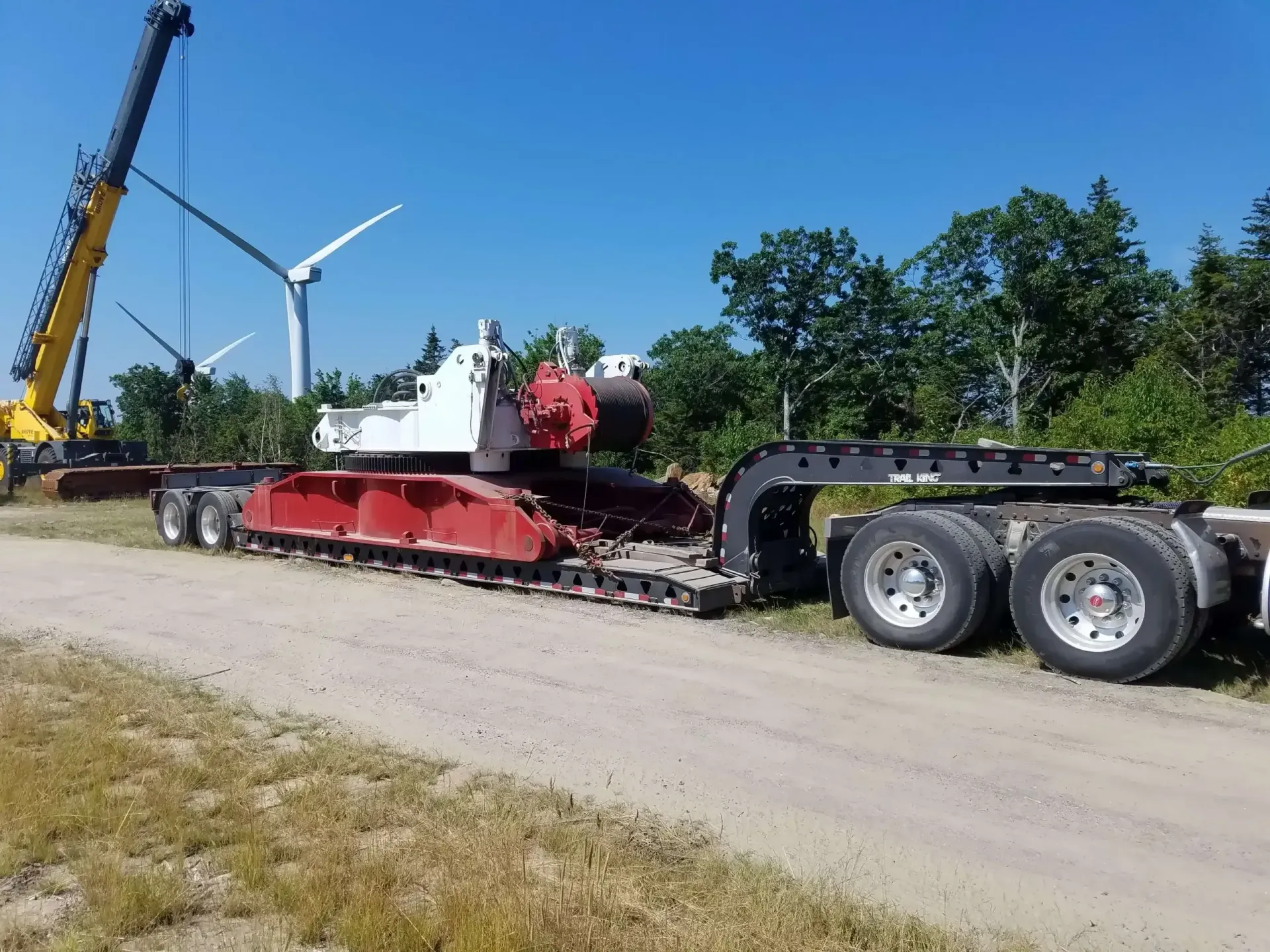 A truck with a crane attached to it is driving down a dirt road.