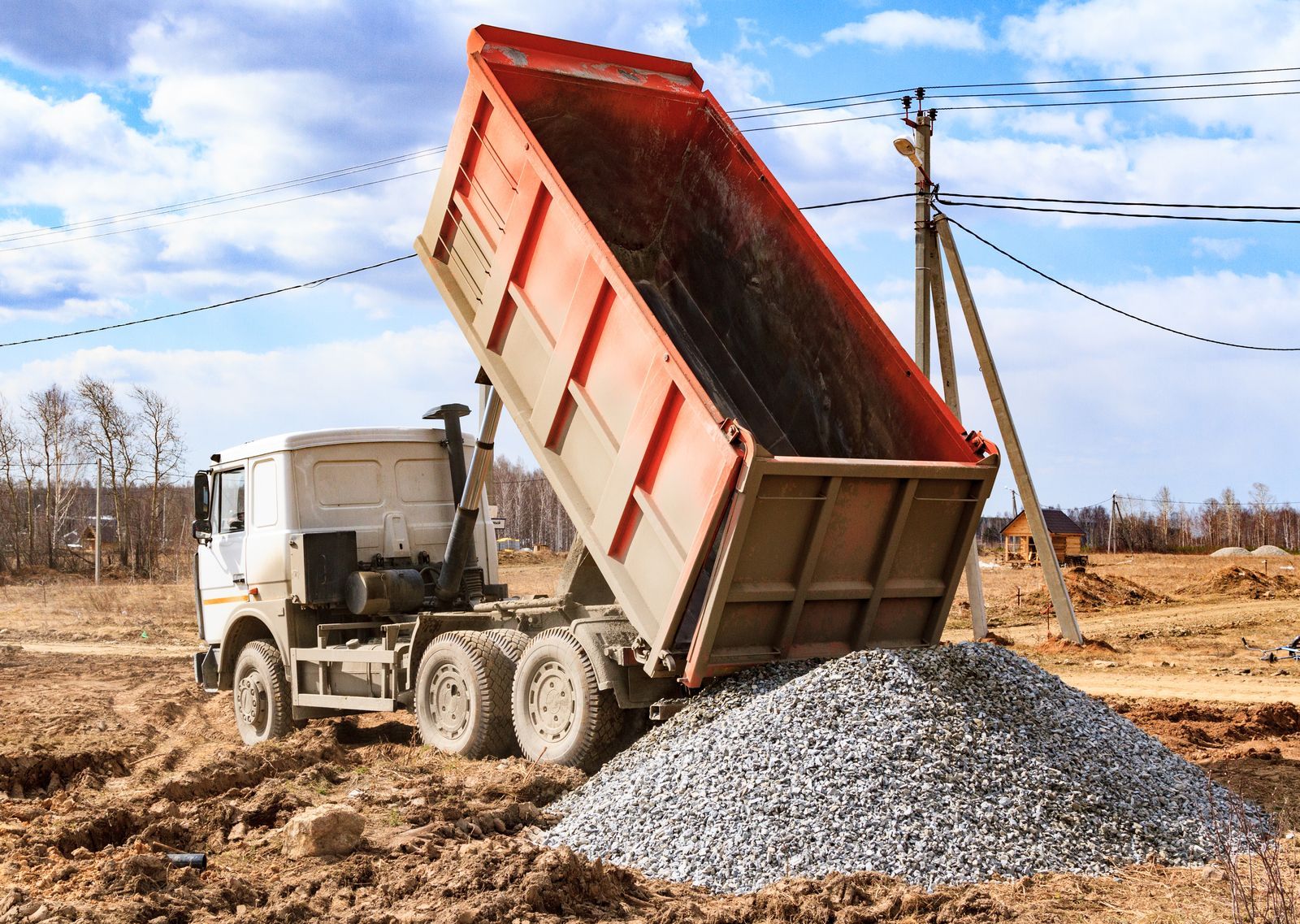 Dump truck with raised bed is unloading gravel on a construction site.