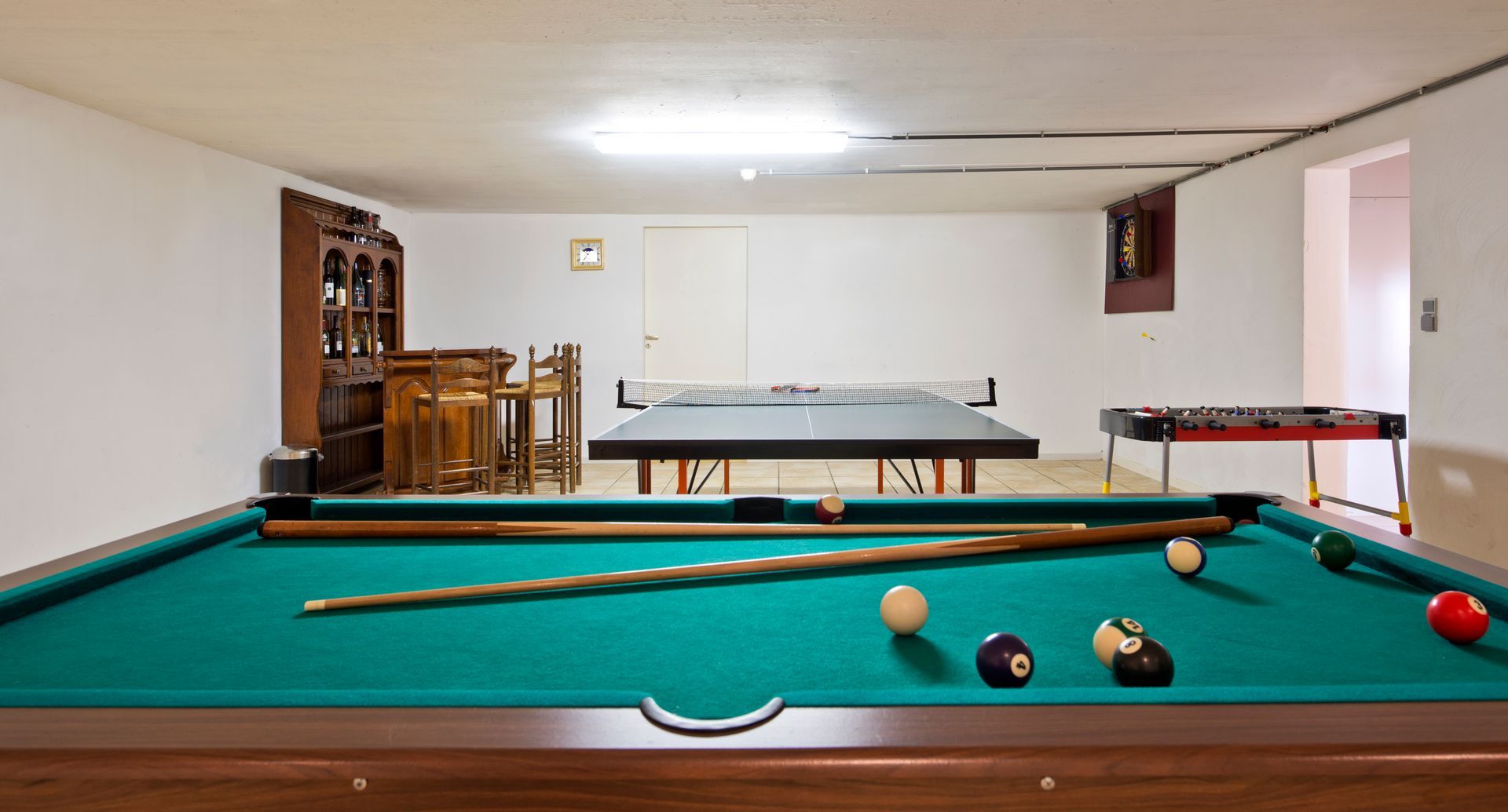 Pool table in a basement game room, with ping pong and foosball tables visible.