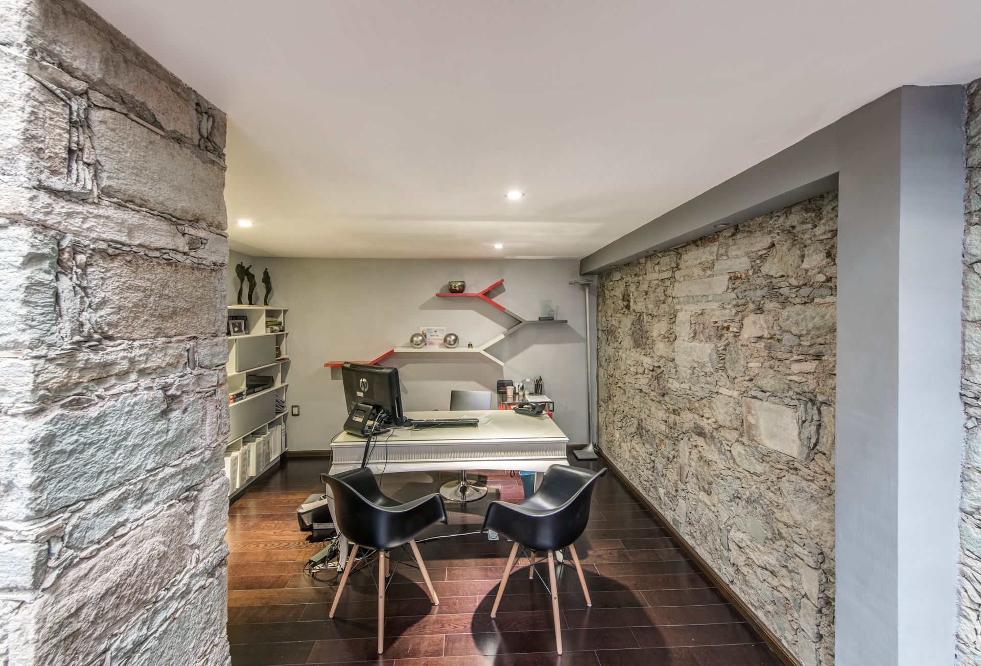 Office with stone walls, black chairs, desk, and a decorative mural.
