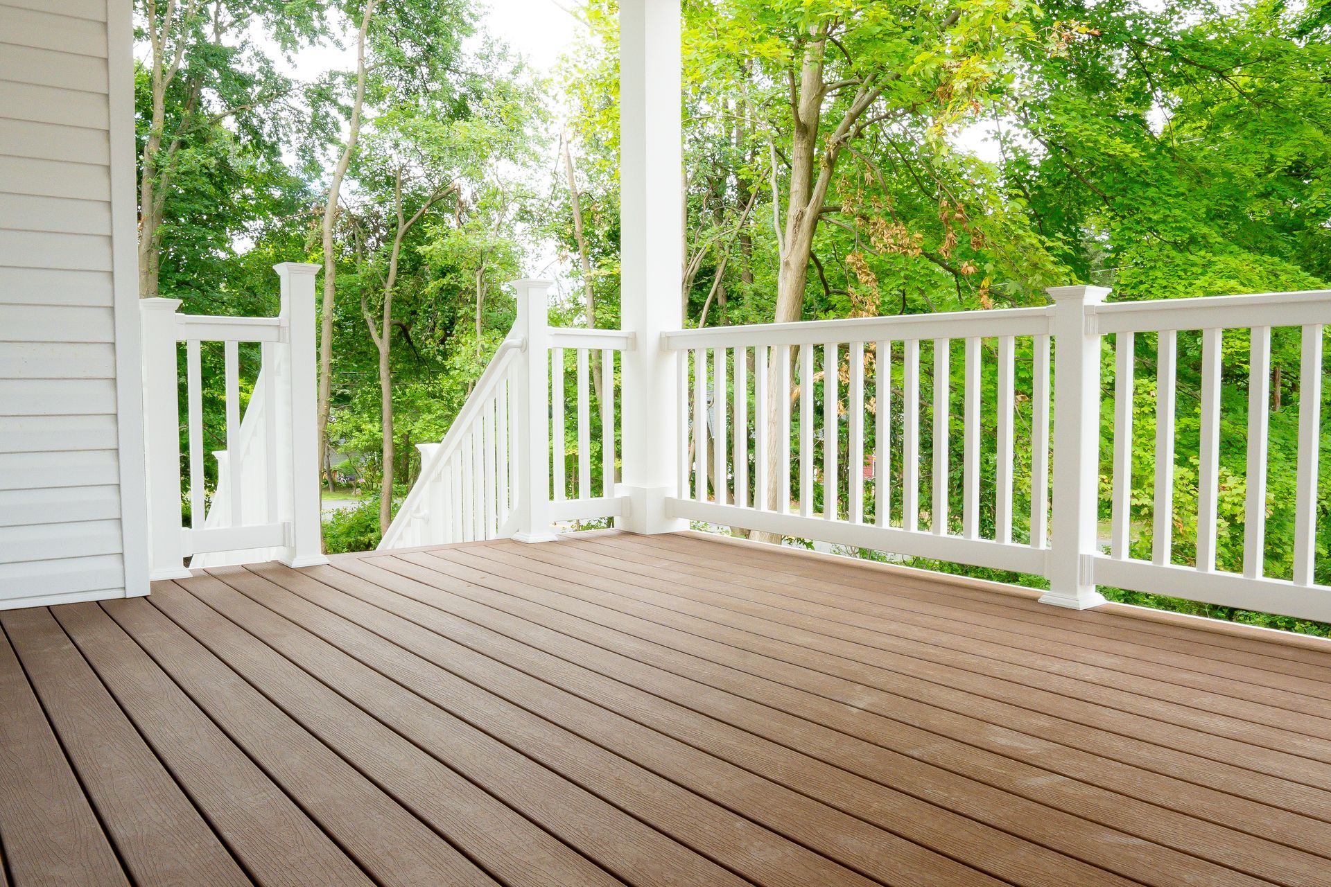 White porch with brown deck overlooking green trees.