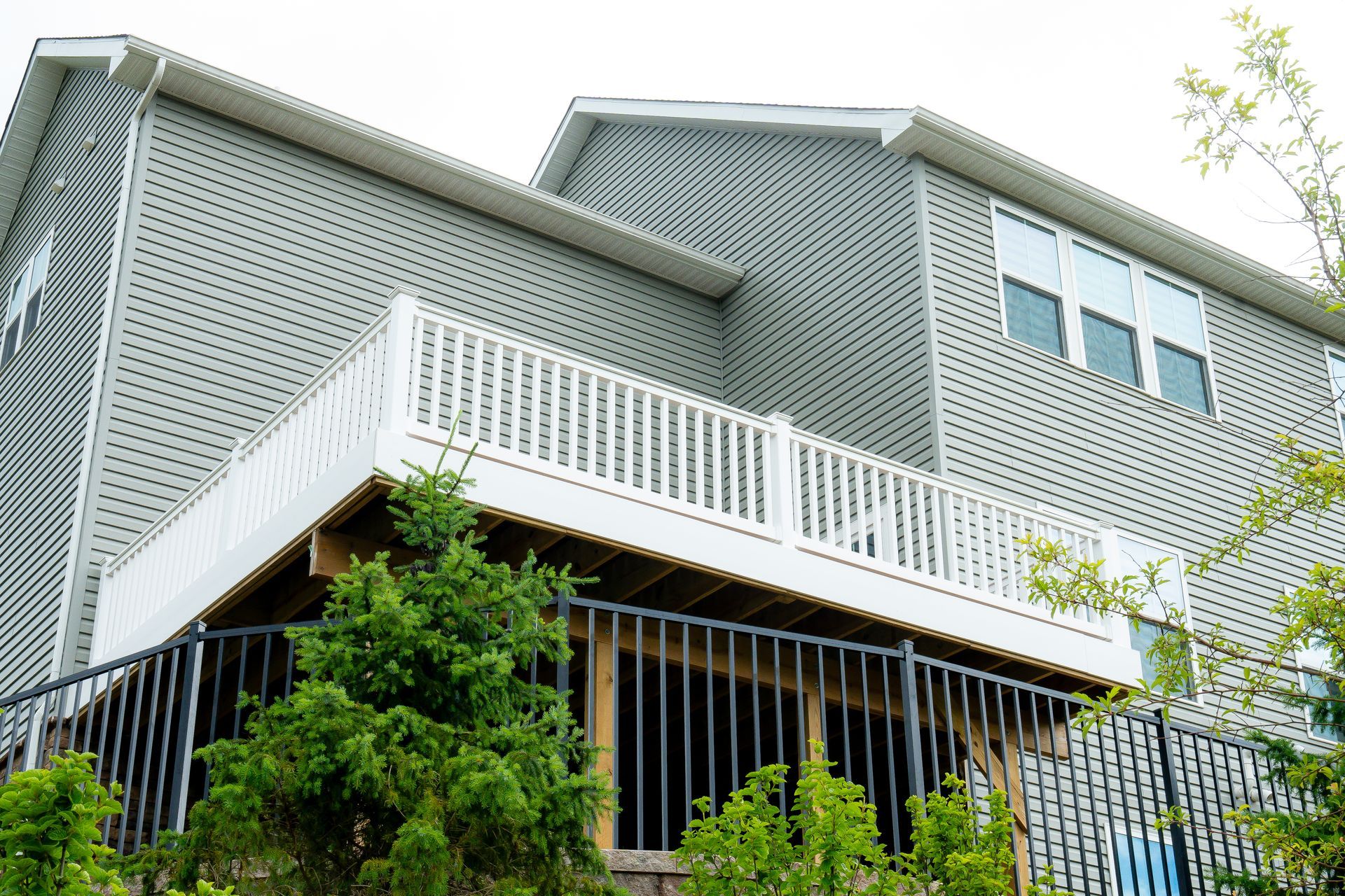 Gray house with white latticework and deck, green trees in front.