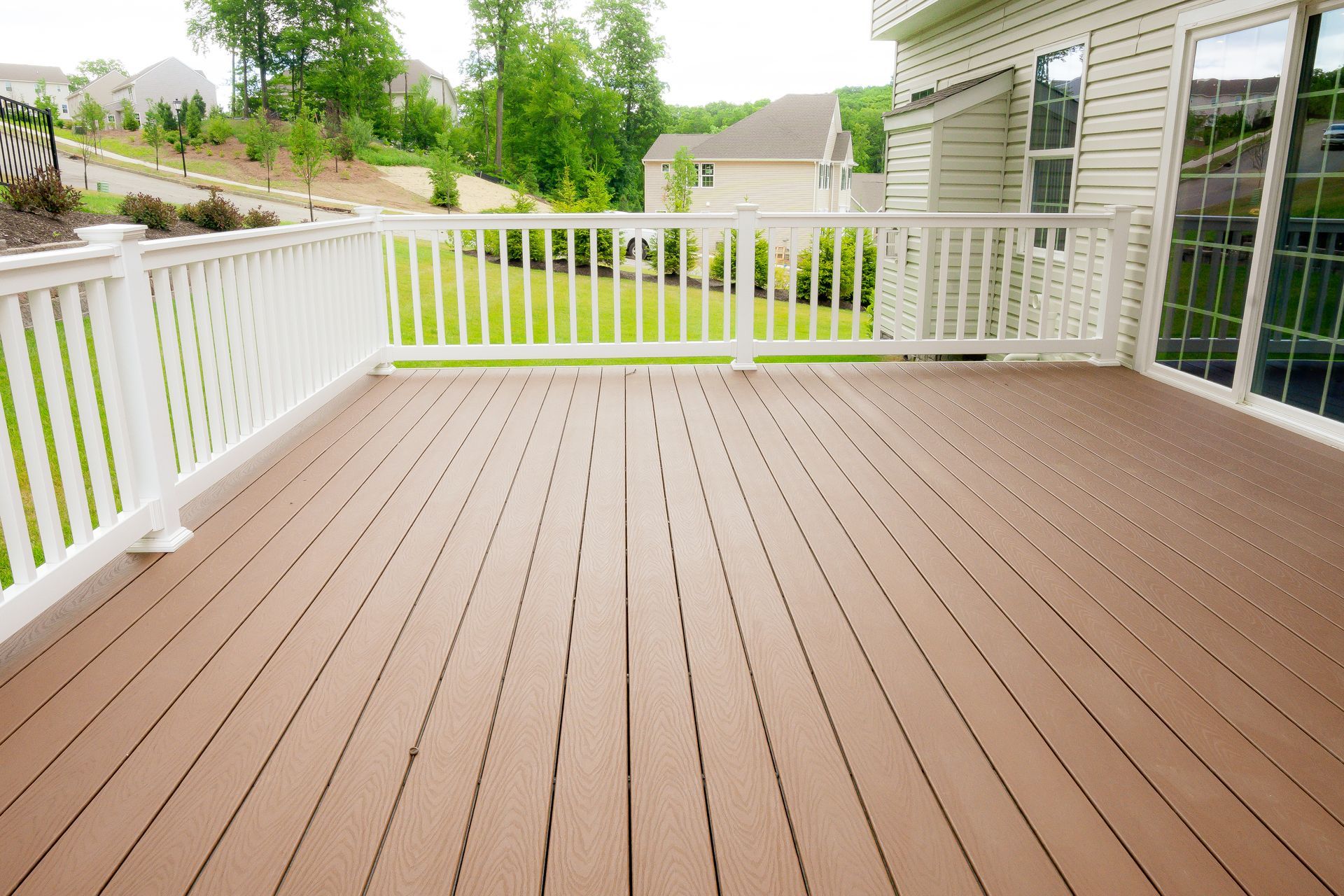 Brown composite deck with white railing overlooking a grassy yard and houses.