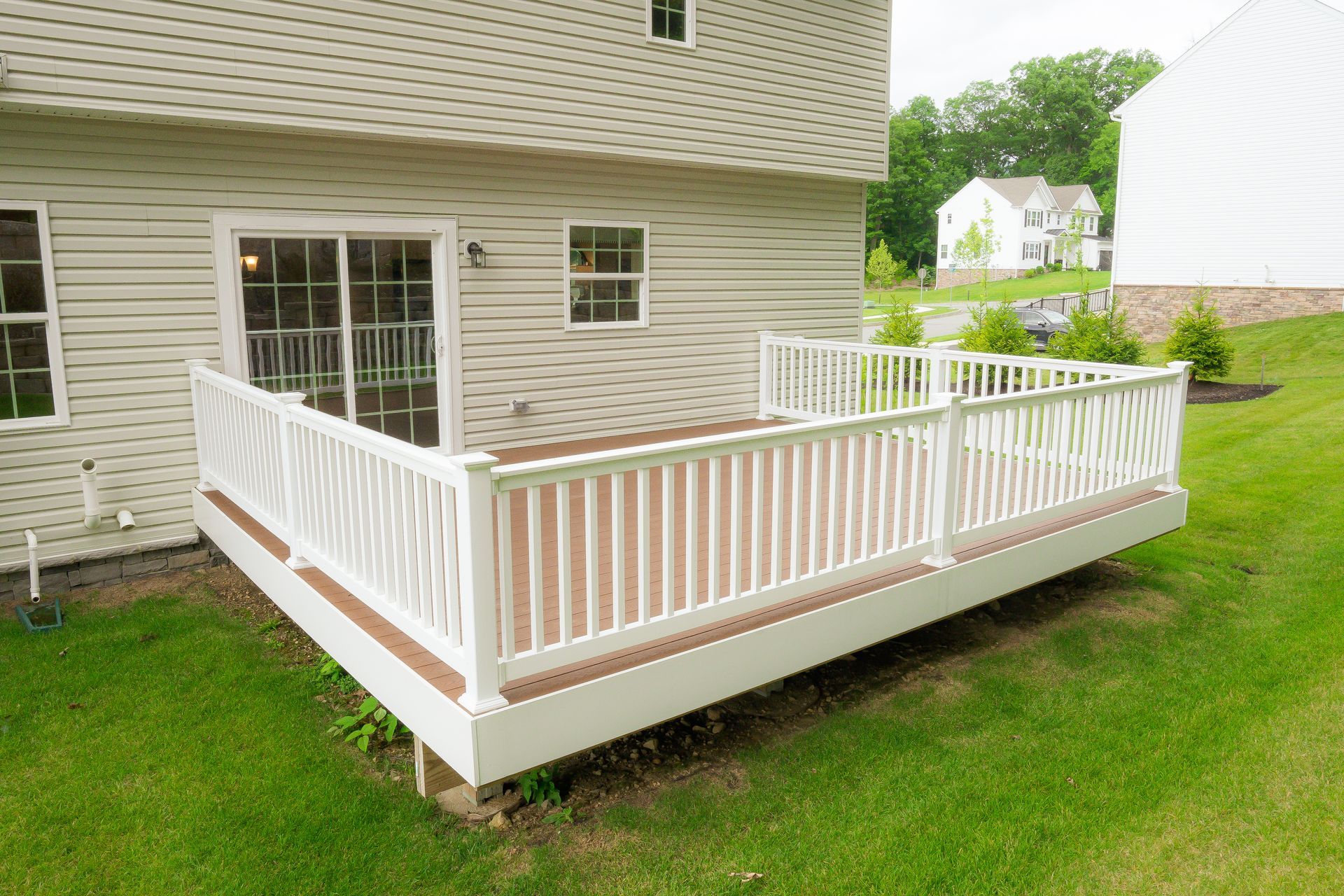 A white deck with railing adjoins a light-colored house, next to green grass.