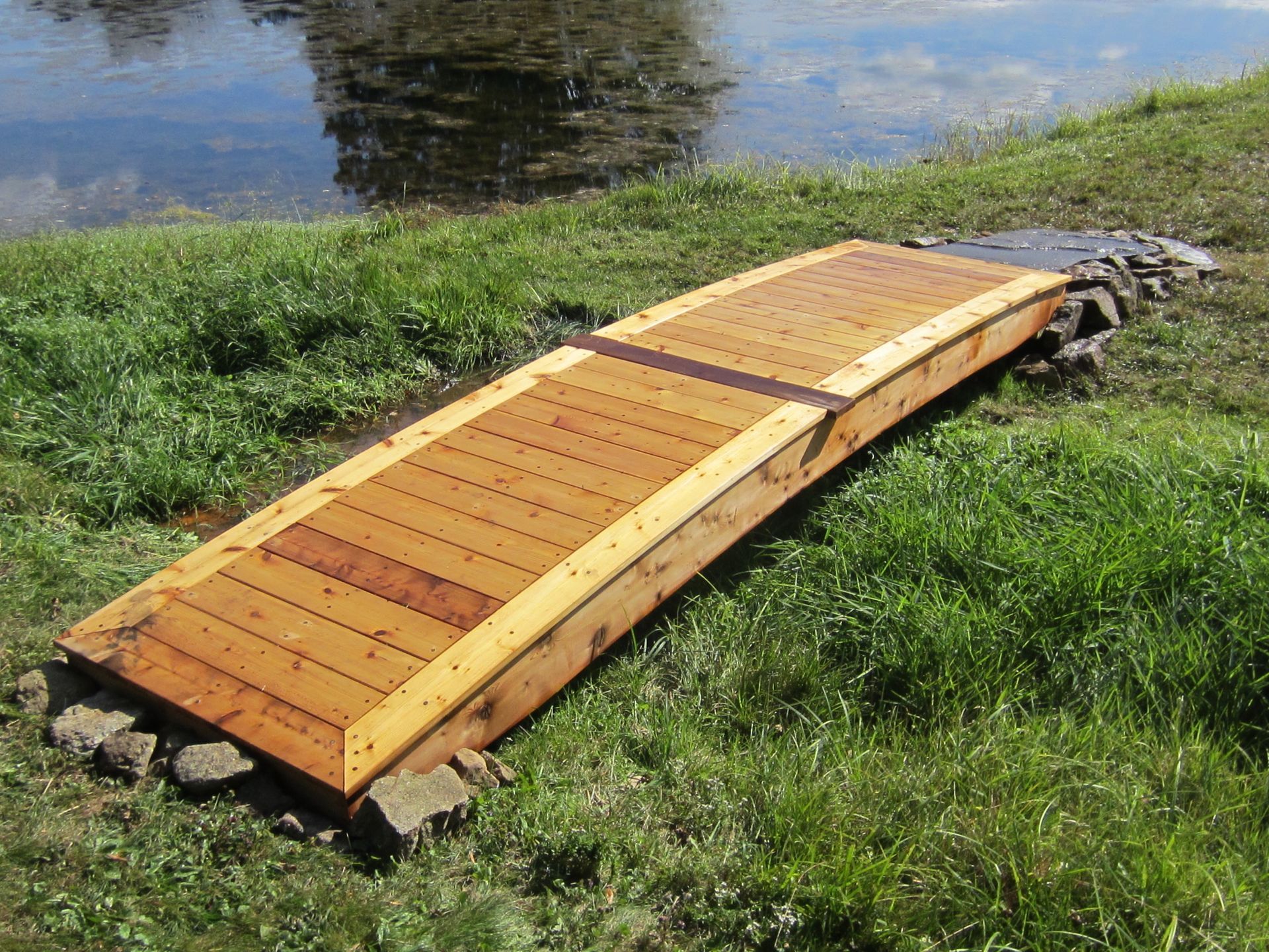 Wooden arched bridge over water and grass.