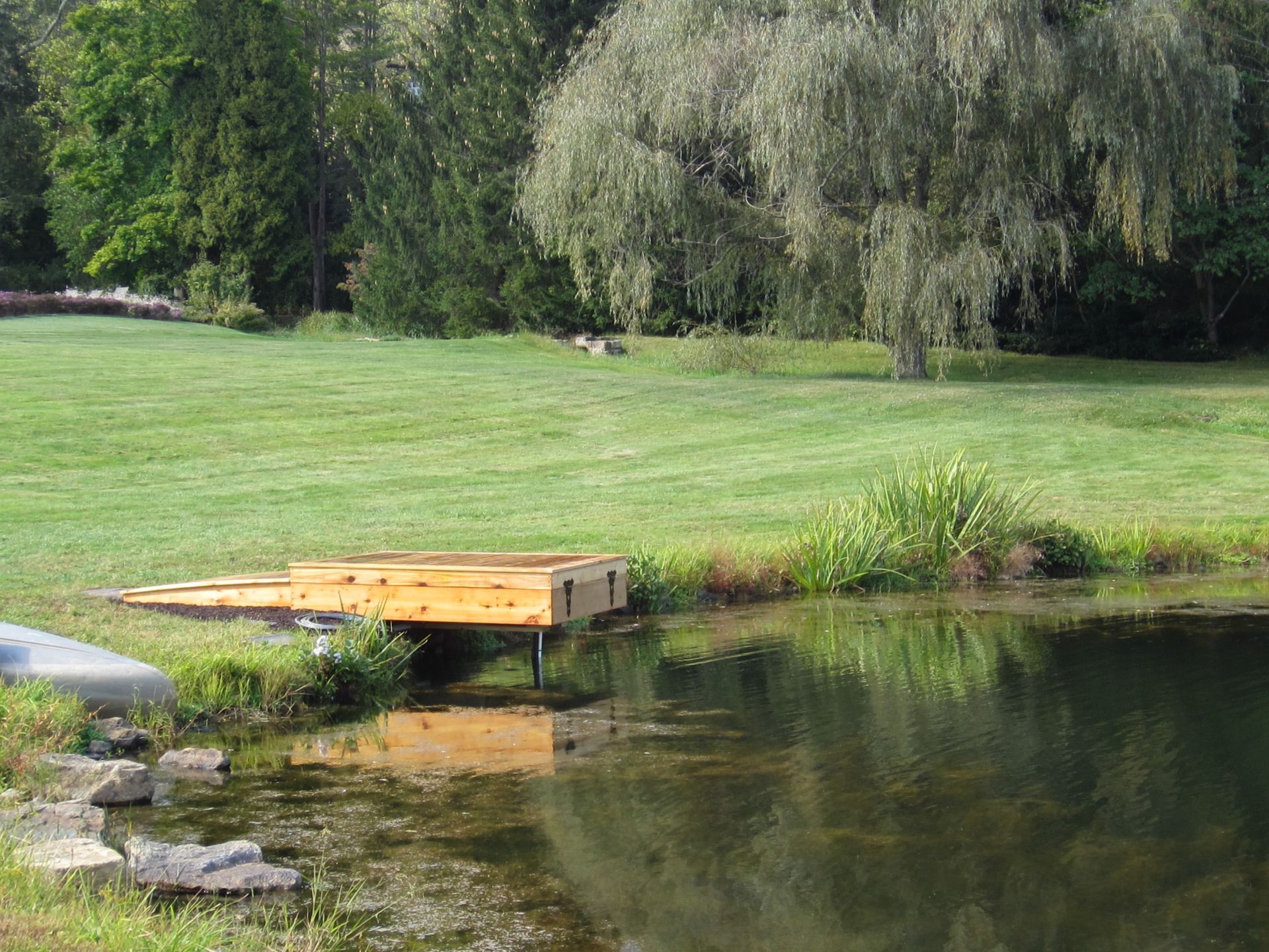 Wooden dock extending into a pond, surrounded by grass and trees.