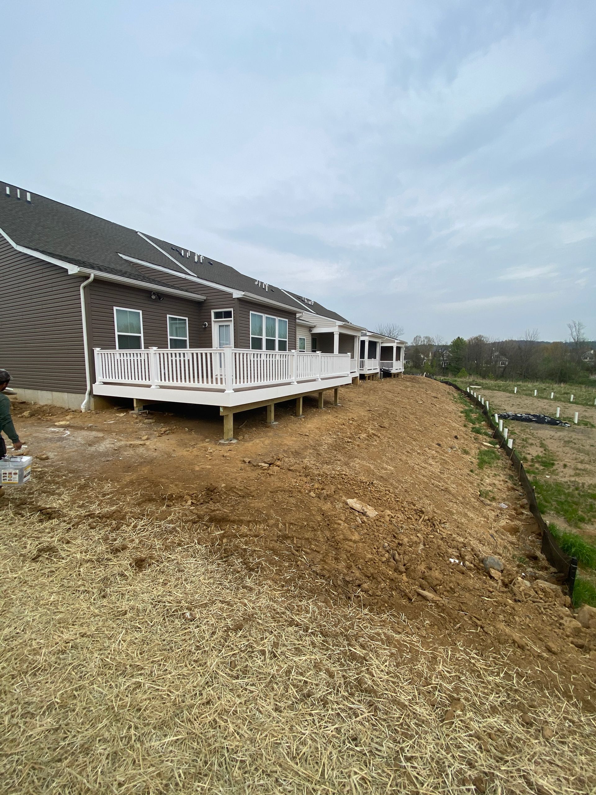 Back of a building with a deck under construction, surrounded by gravel and dirt.