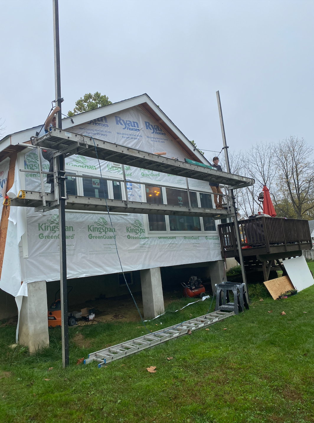 House under construction with scaffolding, wrap, and unfinished deck.
