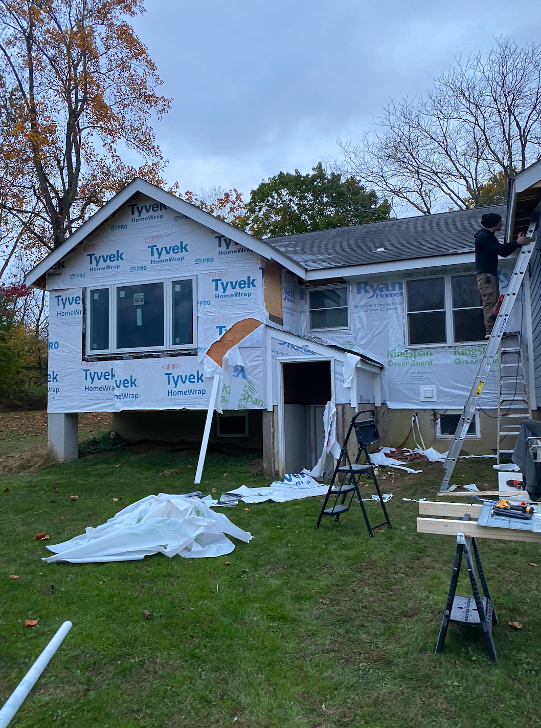 Construction in progress: House exterior with Tyvek wrap, windows, and workers on ladders.