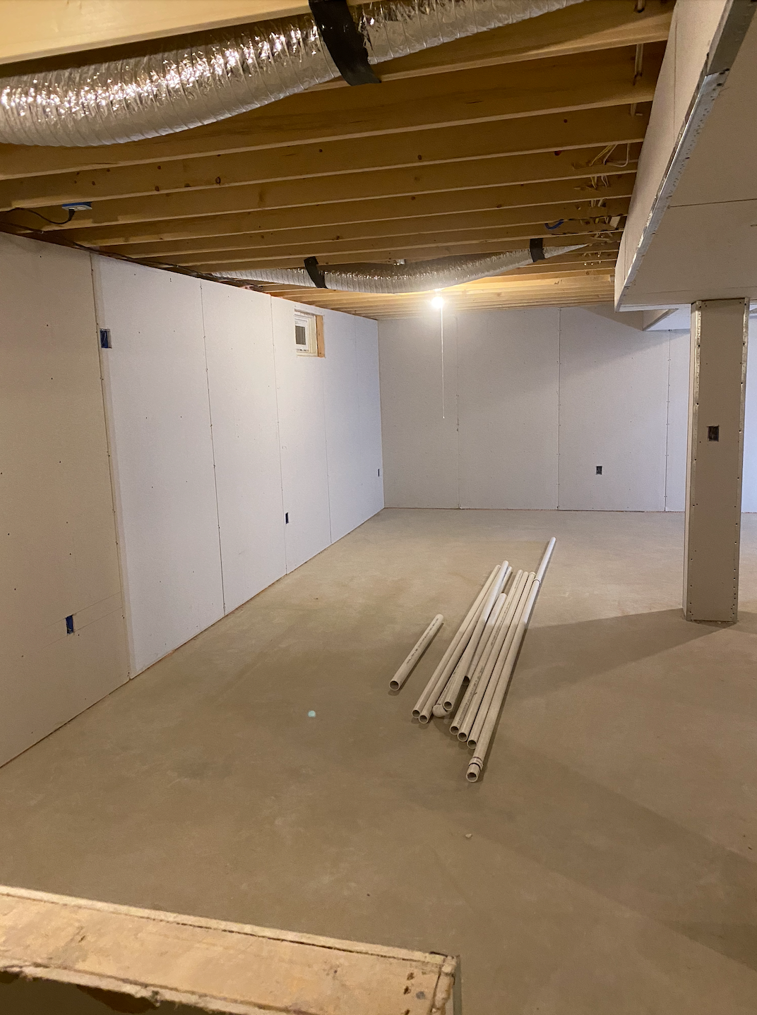 Basement with drywall on walls, ductwork, and wood beams in the ceiling. Trim pieces on the floor.