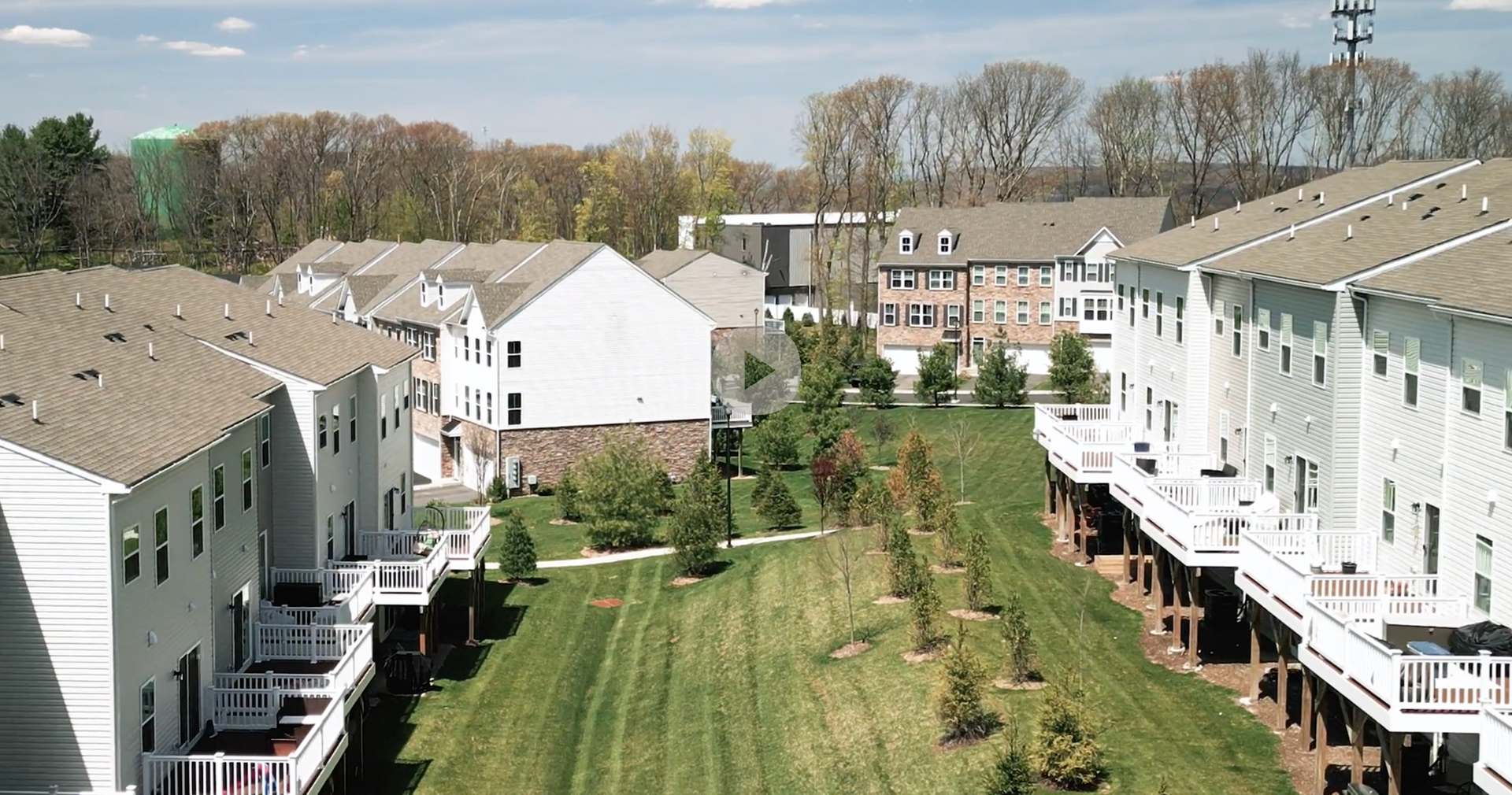 Row of townhouses with a grassy strip in between, trees in the background, and blue sky.