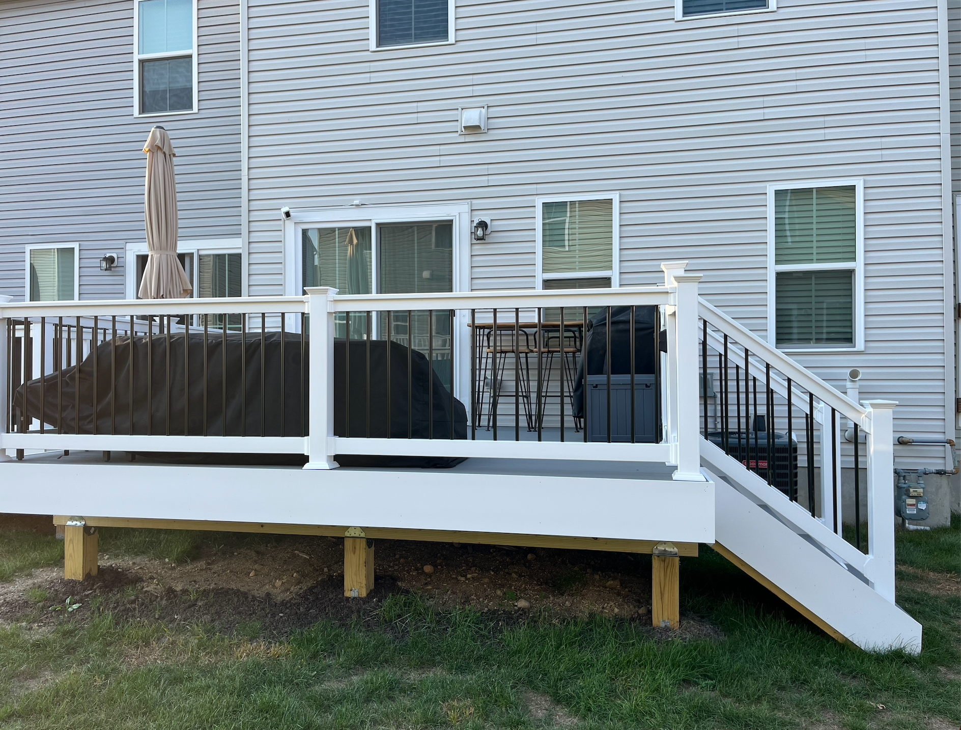 Backyard deck with white railing, black spindles, and a covered grill. The house is in the background.