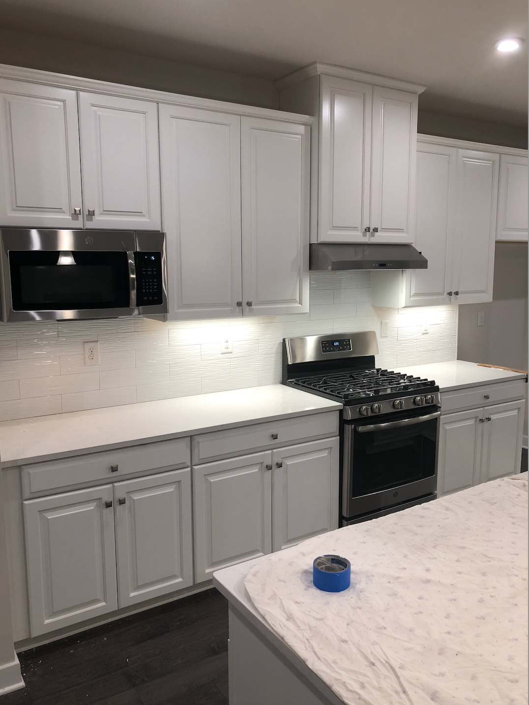 White kitchen with cabinets, appliances, and counters; under cabinet lighting.