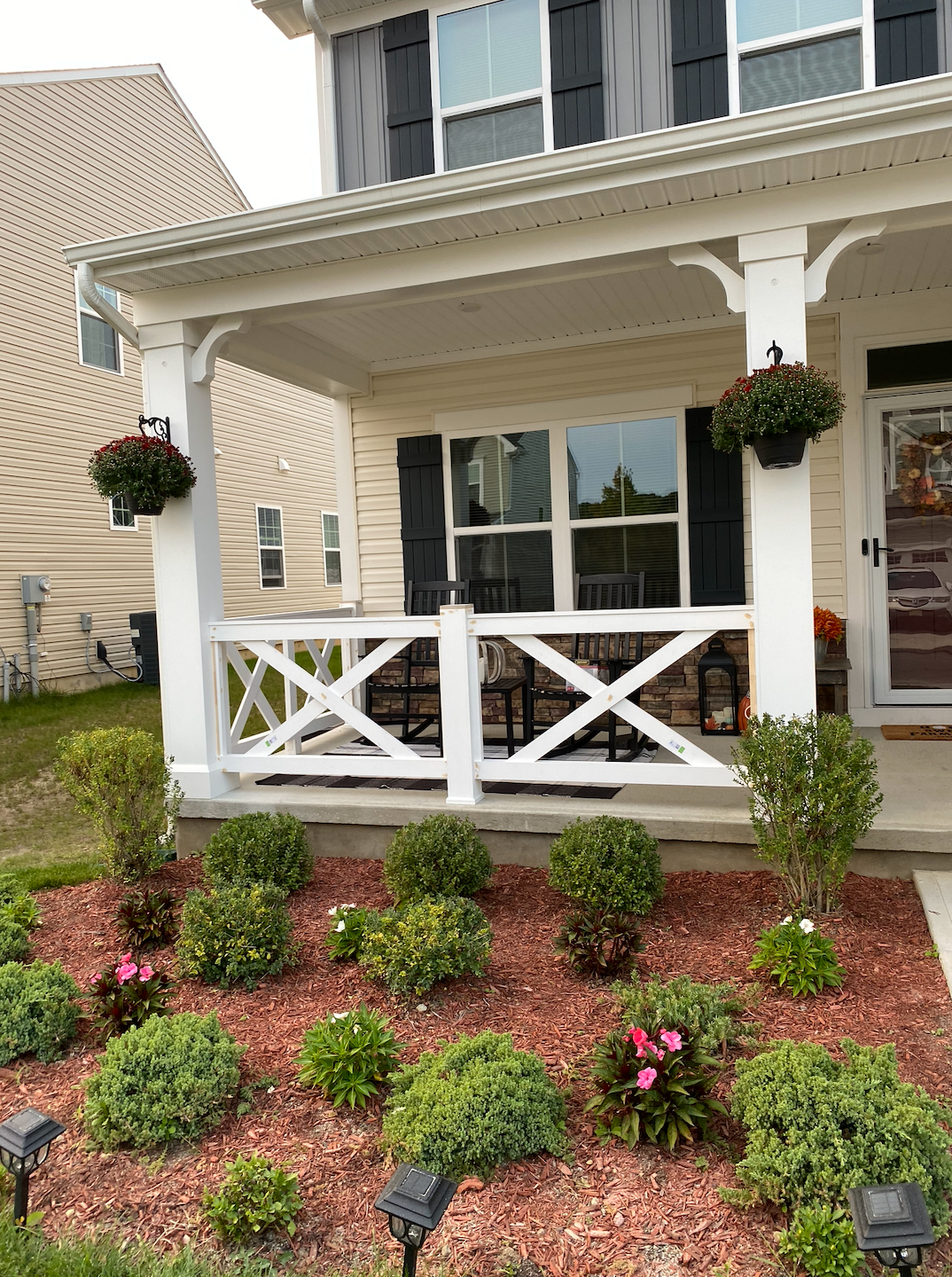 White porch with black shutters, flower boxes, and a red mulch flower bed.