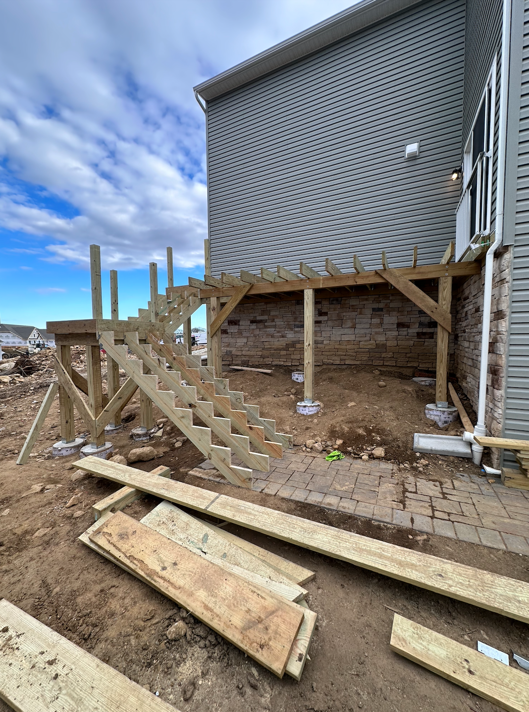 Wooden deck and stairs under construction next to a building with brick foundation.