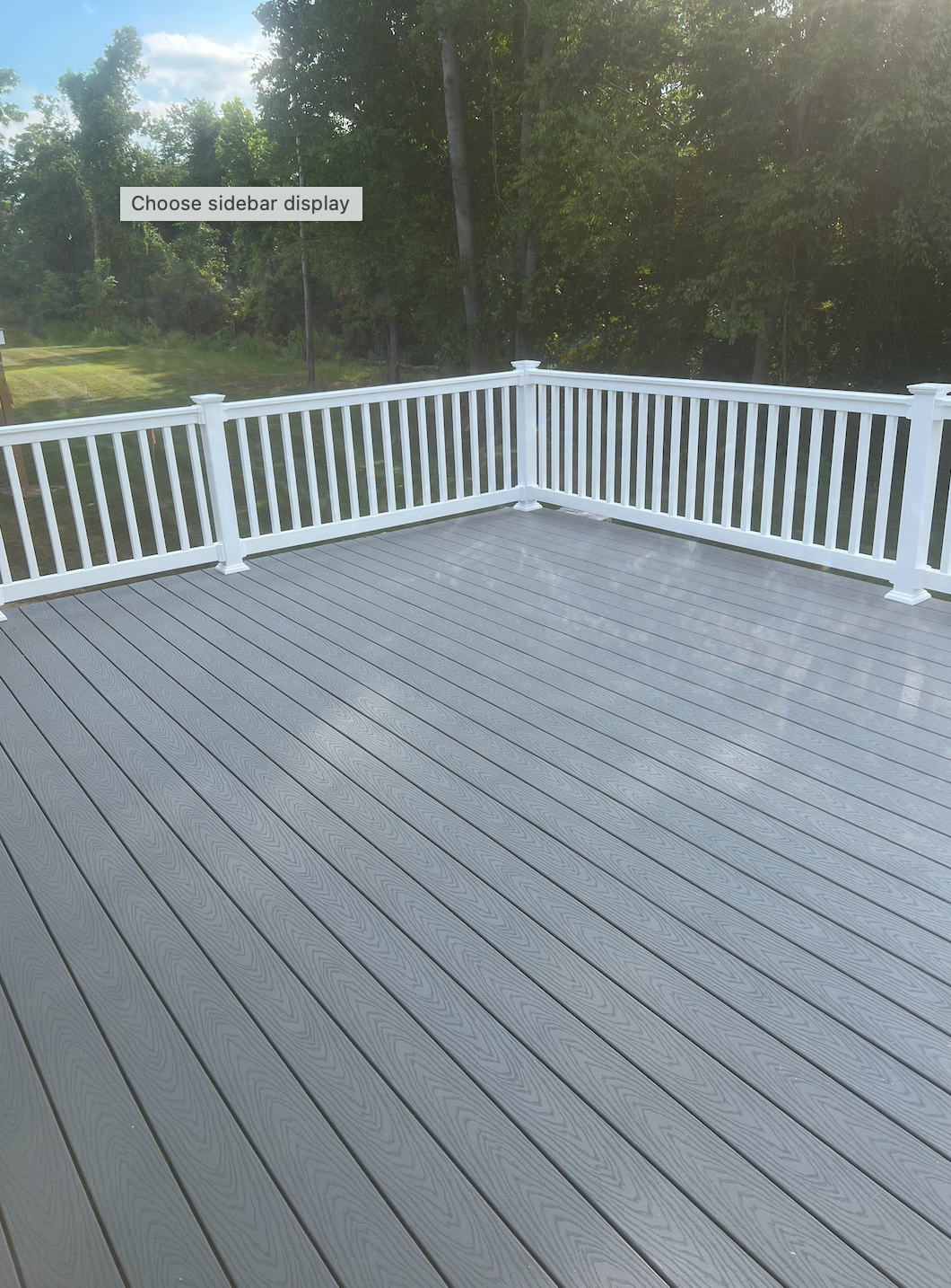 Grey composite deck with white railing in a wooded setting.