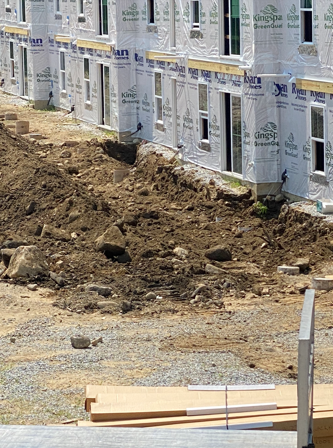 Construction site: row of townhouses under construction with dirt pile in foreground.