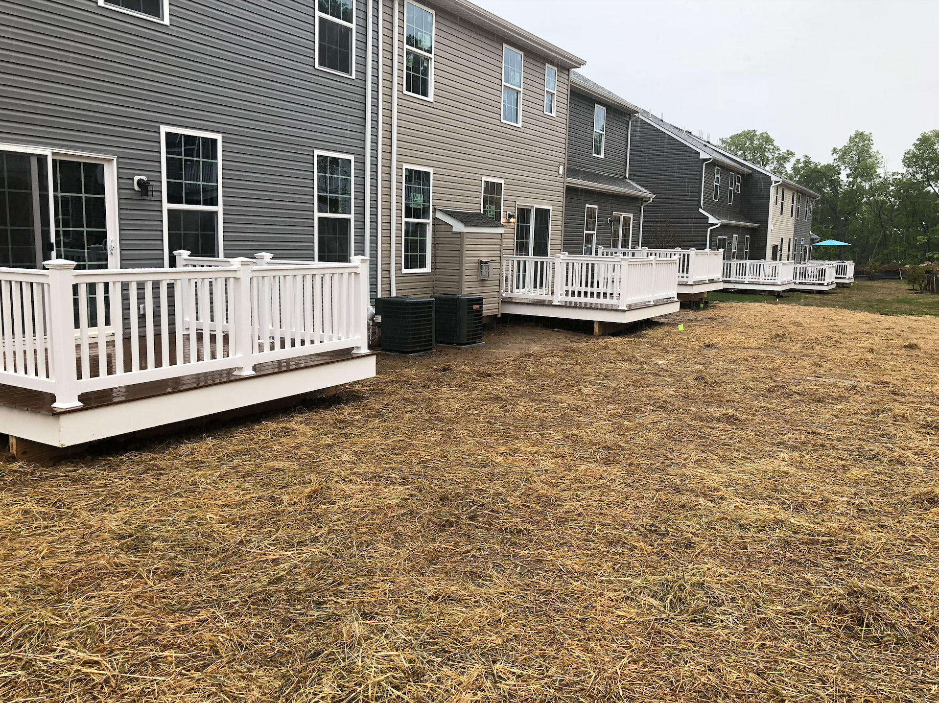 Row of townhouses with white decks and tan-brown lawn.