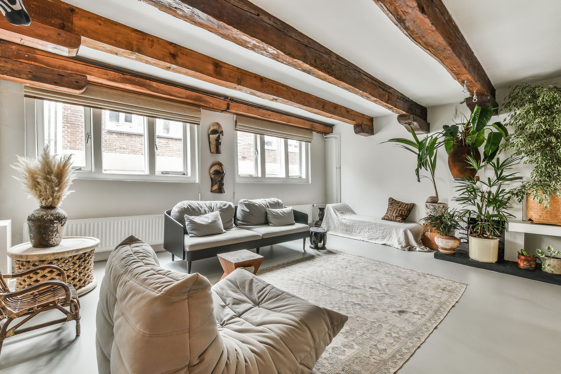 Cozy living room with wood beams, gray furniture, plants, and large rug.