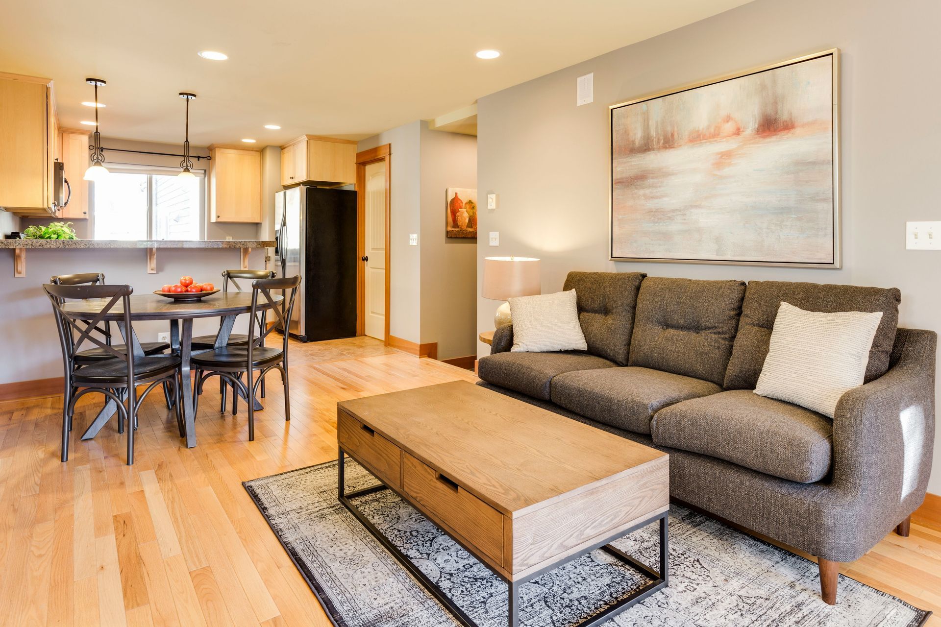 Living room with wood floors, a gray sofa, a wooden coffee table, and a dining area with a round table and chairs.