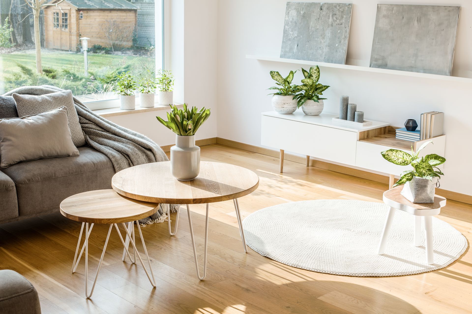 Living room with wooden coffee tables, gray sofa, plants, rug, and white decor.
