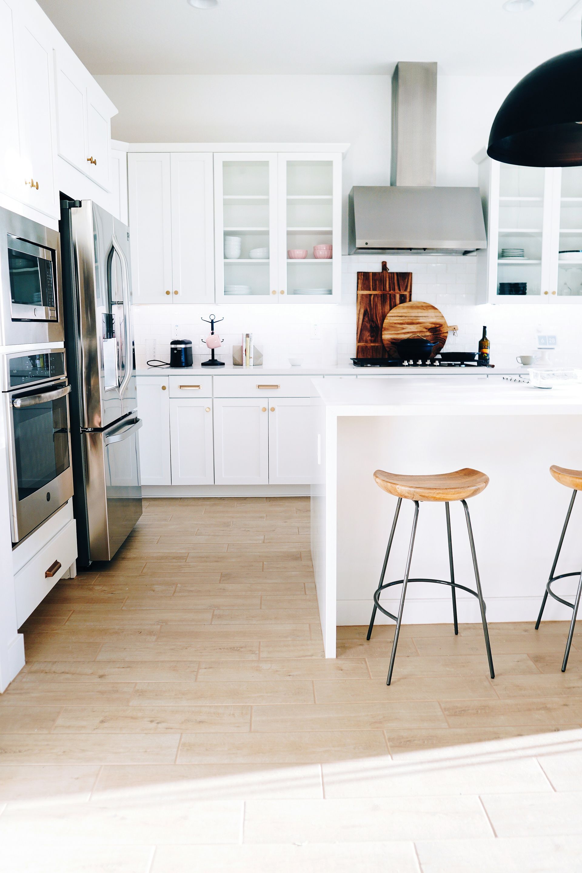 White modern kitchen with stainless steel appliances, wooden stools, and light wooden floor.